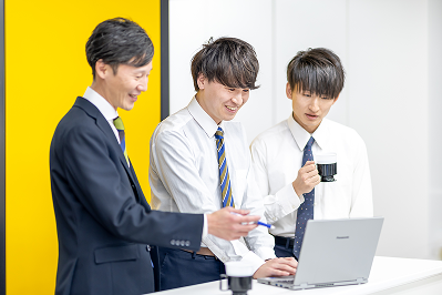 ノートパソコンの画面を見ながら笑顔で談笑する男性スタッフたち