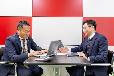テーブルを挟んでノートパソコンを見ながら、笑顔で打ち合わせをする男性スタッフ2名