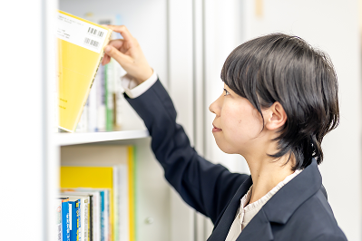 オフィス内の本棚から資料(専門書)を取り出す女性スタッフ